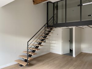 Escalier droit avec un limon central en acier menant vers une mezzanine